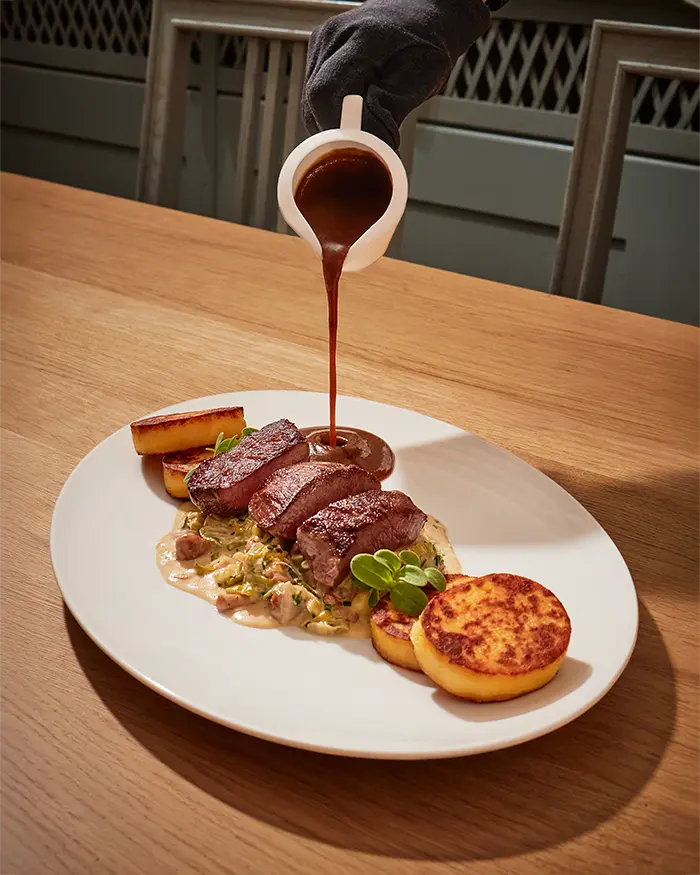 gravy getting poured over a meat dish with mushroom cream sauce and potato fritters