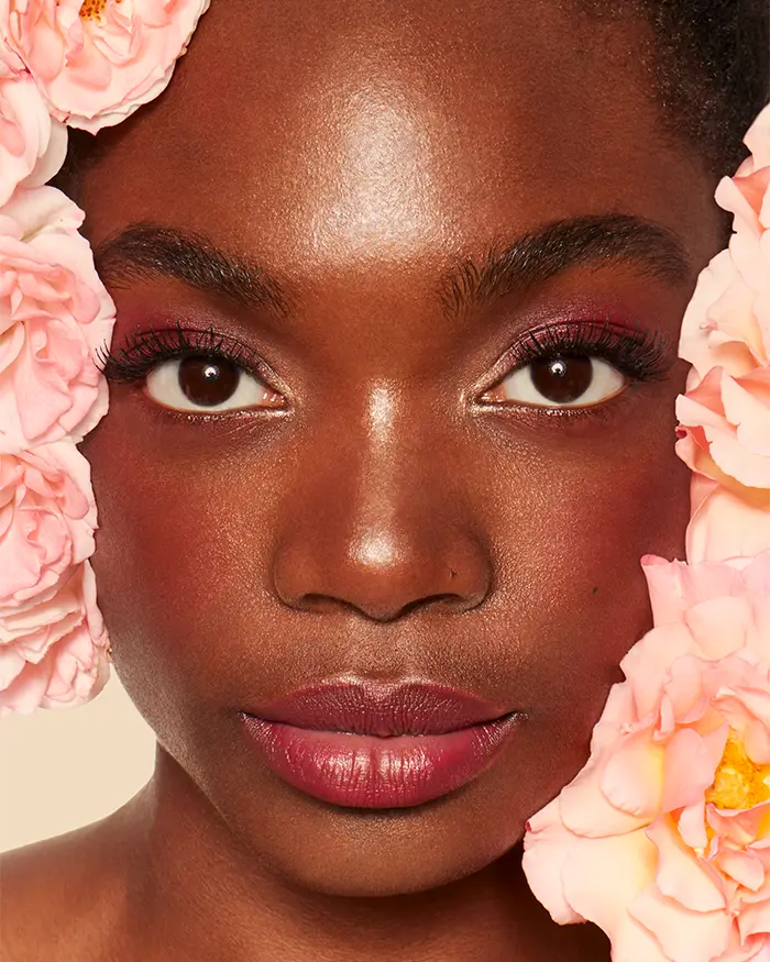 close up of a black womans face surrounded by peachy roses with pink blush 