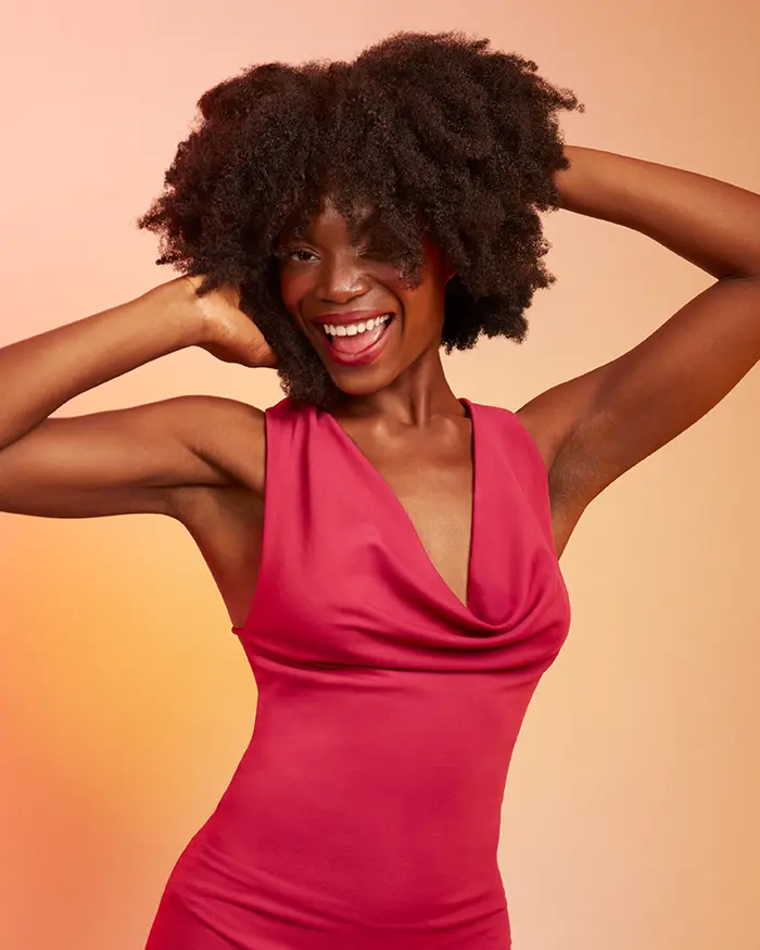 Black woman playing with her natural afro curls wearing a pink dress