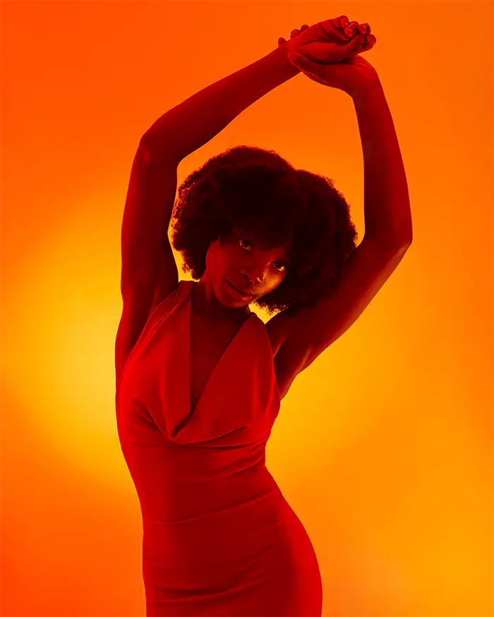 Black woman with natural afro curls in a orange sunset light with her arms above her head